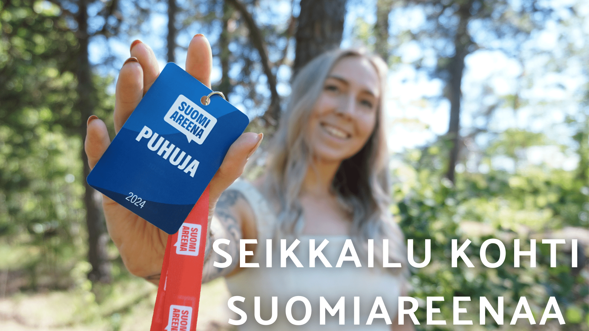 Taustalla vaaleatukkainen nainen, joka pitää kädessä korttia, jossa lukee "SuomiAreena Puhuja"